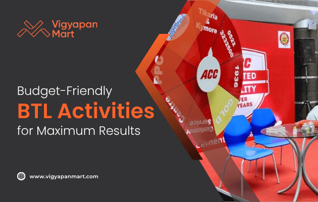 A promotional display with a red spinning prize wheel, blue chairs, and a glass table. Text reads: “Budget-Friendly BTL Activities for Maximum Results” with the Vigyapan Mart logo and website.