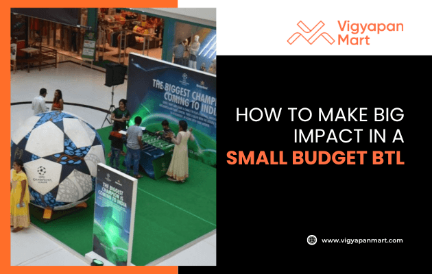 A mall activation setup with a giant soccer ball, foosball table, and banners. Text reads, How to make big impact in a small budget BTL. Vigyapan Mart logo and website are displayed.
