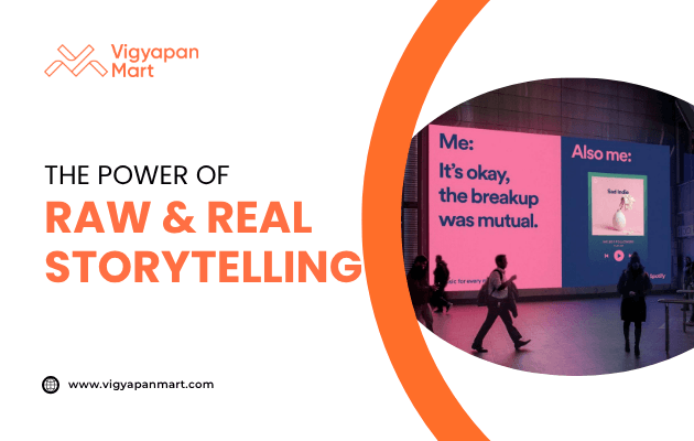 Digital billboard in a public space displaying a Spotify ad with bold pink and blue design, featuring text “Me: It’s okay, the breakup was mutual. Also me:” alongside a music playlist. Overlay text reads “The Power of Raw & Real Storytelling” with Vigyapan Mart branding, emphasizing authentic storytelling in advertising.