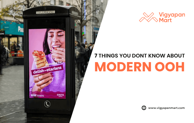 Digital out-of-home (OOH) advertising display on a city street shows a woman eating food with the text “suitable for delish-etarians.” On the right side, Vigyapan Mart branding appears with the headline “7 Things You Don’t Know About Modern OOH” and website link www.vigyapanmart.com