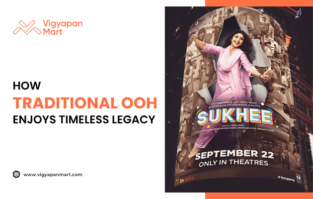 Outdoor advertising poster for the movie “Sukhee” displayed on a curved billboard, featuring a woman in a pink outfit with release date “September 22 Only in Theatres.” On the left side, Vigyapan Mart branding with the text “How Traditional OOH Enjoys Timeless Legacy” and website www.vigyapanmart.com