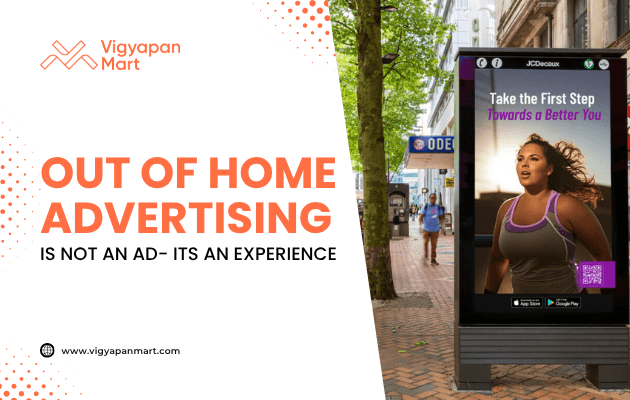 Digital out-of-home advertising display on a busy shopping street shows a fitness ad with a woman in workout clothes and the text “Take the First Step Towards a Better You.” On the left, Vigyapan Mart branding with the headline “Out of Home Advertising is Not an Ad – It’s an Experience” and website www.vigyapanmart.com