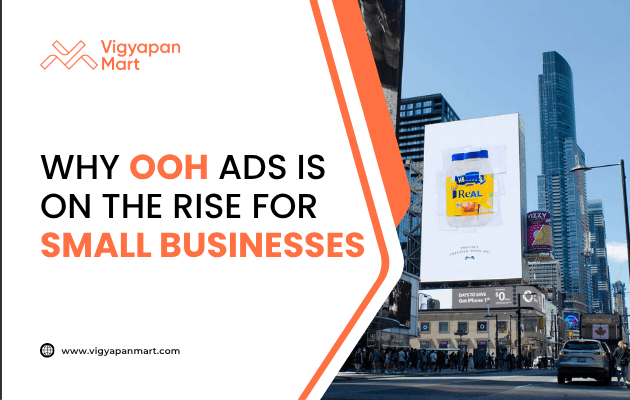Large outdoor billboard in a city center displays an ad for a product with the word “Real.” On the left side, Vigyapan Mart branding with text “Why OOH Ads is on the Rise for Small Businesses” and website www.vigyapanmart.com