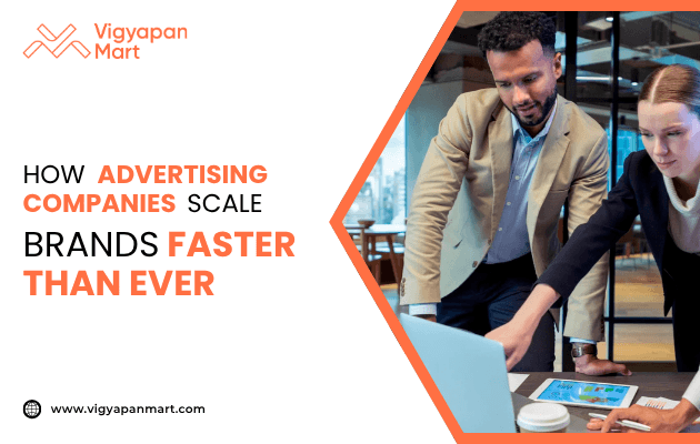 Two professionals in a modern office setting discuss a project while looking at a laptop and tablet. On the left, Vigyapan Mart branding with the text “How Advertising Companies Scale Brands Faster Than Ever” and website www.vigyapanmart.com