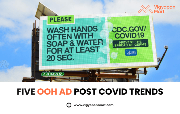 Large outdoor billboard displays a CDC COVID-19 safety message: “Wash hands often with soap & water for at least 20 sec.” promoting hygiene awareness. Below, Vigyapan Mart branding with the headline “Five OOH Ad Post Covid Trends” and website www.vigyapanmart.com