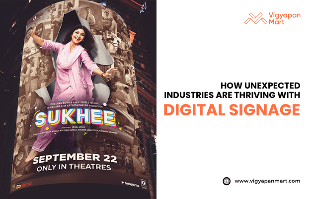 Vigyapan Mart graphic featuring a digital signage display for the movie “Sukhee,” showing a smiling woman in a pink outfit with release date “September 22 Only in Theatres.” Right side text reads “How Unexpected Industries Are Thriving with Digital Signage,” with “Digital Signage” highlighted in orange. Vigyapan Mart logo and website are shown.