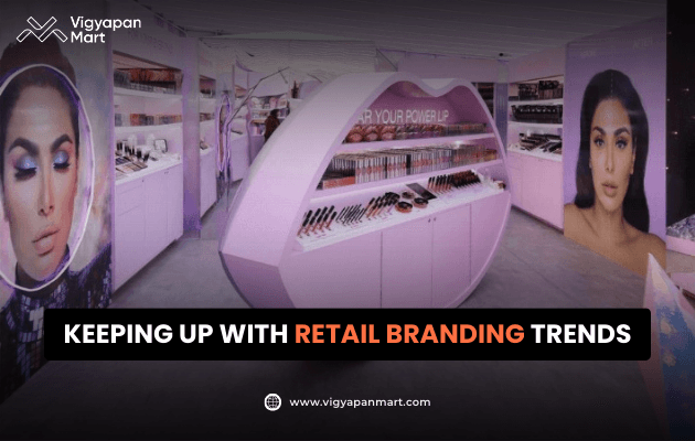 Vigyapan Mart graphic showcasing a modern cosmetics retail store with pink-themed displays, makeup counters, and large model posters. Text overlay reads “Keeping Up with Retail Branding Trends.” Vigyapan Mart logo and website are shown.