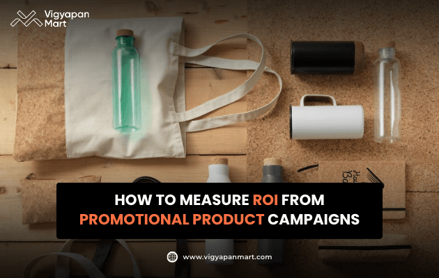 Vigyapan Mart creative featuring eco-friendly promotional items like tote bags, bottles, mugs, and notebooks. Text overlay reads “How to Measure ROI from Promotional Product Campaigns.” Vigyapan Mart logo and website included.