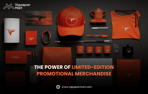Flat lay of limited-edition promotional merchandise including branded cap, notebook, tote bag, mugs, pens, keychains, and stationery in bold orange and black theme with logo imprint. Marketing banner text reads 'The Power of Limited-Edition Promotional Merchandise' by Vigyapan Mart, showcasing exclusive brand identity products.