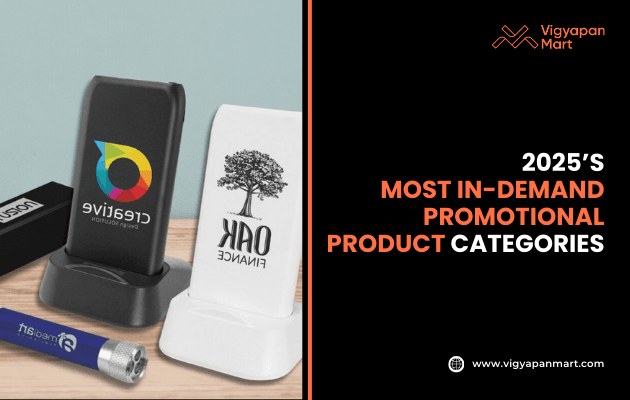 Modern promotional products for 2025 including branded wireless charging stands with 'Creative' and 'Oak Finance' logos, along with a flashlight on wooden surface. Marketing banner text reads '2025’s Most In-Demand Promotional Product Categories' by Vigyapan Mart, showcasing trending merchandise for businesses.