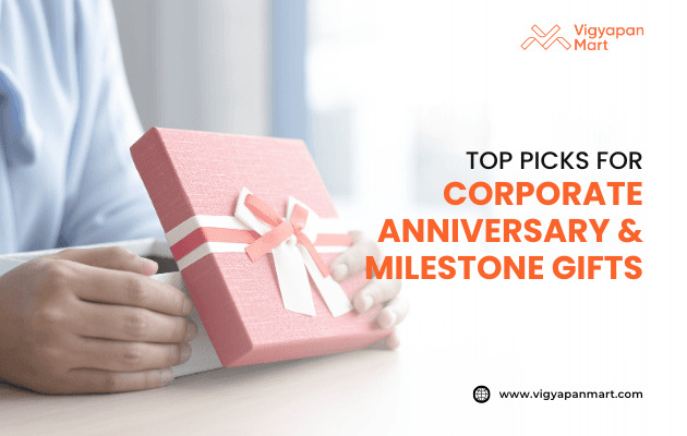 Professional banner featuring hands holding a pink corporate gift box with white ribbon, promoting 'Top Picks for Corporate Anniversary & Milestone Gifts' by Vigyapan Mart, emphasizing business gifting ideas, employee recognition, and milestone celebrations.