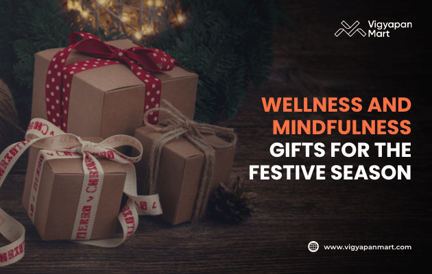 Festive gift boxes wrapped in brown paper with ribbons and twine, placed near greenery and lights, with text: Wellness and mindfulness gifts for the festive season. Vigyapan Mart branding and website shown.