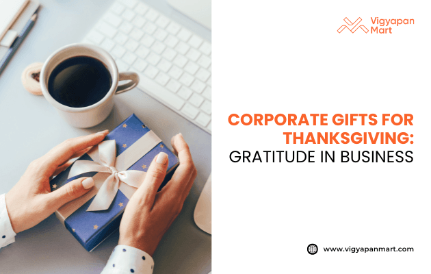 Person holding a blue gift box with white ribbon next to a cup of coffee on a desk, with text: Corporate gifts for Thanksgiving: Gratitude in business. Vigyapan Mart branding and website shown.
