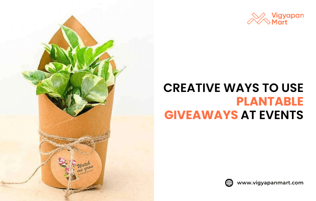 Small green plant wrapped in eco-friendly brown paper with twine and a round tag that reads “Watch me grow.” Text on the right says: “Creative ways to use plantable giveaways at events” with Vigyapan Mart logo and website www.vigyapanmart.com. Eco-friendly event giveaway concept.