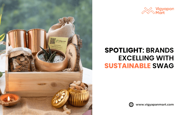 Wooden gift box with eco-friendly sustainable swag items including copper tumblers, a small potted plant, jute pouch, healthy snacks, and natural candles. Text on the right reads: “Spotlight: Brands excelling with sustainable swag” with Vigyapan Mart logo and website www.vigyapanmart.com.Eco-conscious corporate gifting concept.