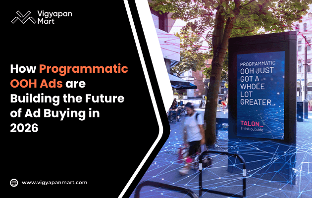 Outdoor digital ad display stating 'Programmatic OOH just got a whole lot greater.' Trees and people walking briskly are in the background. The ad suggests advancement in advertising technology by 2026. Vigyapan Mart branding and a website link are visible on a black and white graphic on the left.