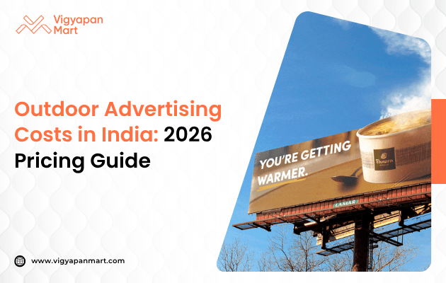 An image shows a large outdoor billboard set against a blue sky, featuring a steaming coffee cup with the text “You’re getting warmer.” Nearby text reads “Outdoor Advertising Costs in India: 2026 Pricing Guide” by Vigyapan Mart, along with their logo, conveying a warm and insightful marketing tone.